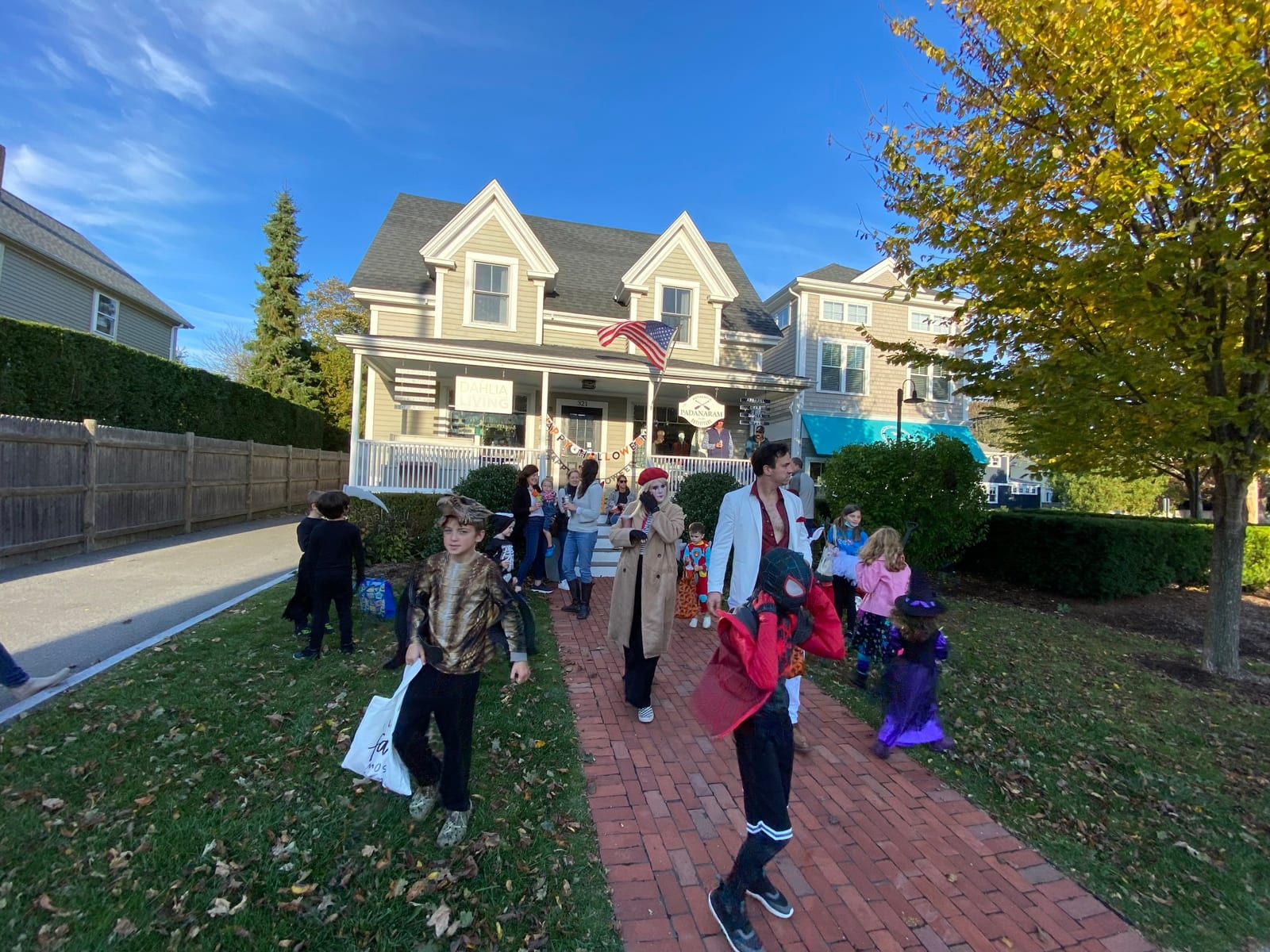 Trick-or-treaters in costume on the brick walk in front of the Padanaram village shops on a bright fall afternoon.